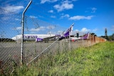 Two purple and white planes on a tarmac, seen through a chainlink fence.