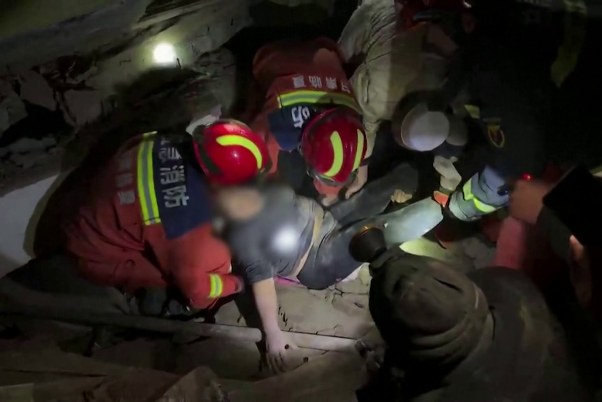 Emergency workers lift up a woman amidst rubble. 