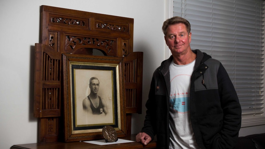 Greg Antcliff stands next to furniture holding a portrait of James Antcliff.