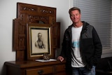 Greg Antcliff stands next to furniture holding a portrait of James Antcliff.