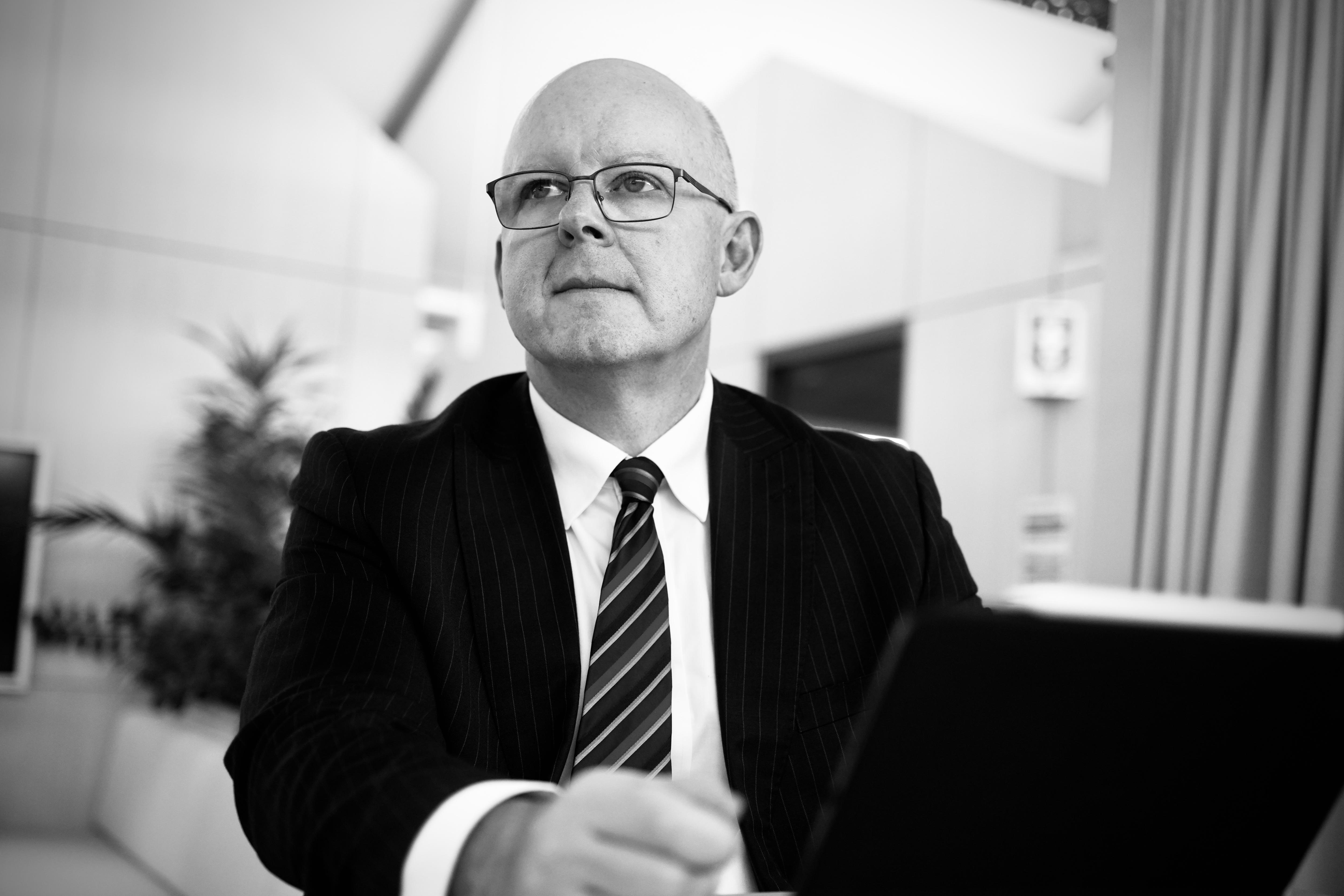 Black and white photo of a man wearing a suit, tie and glasses.