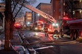 A large ladder reaches at the top of the building with a firefighter in front of it