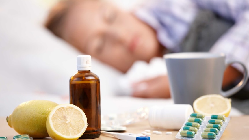 A woman sleeps with a mug, lemons, and cold and flu medication nearby.