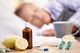 A woman sleeps with a mug, lemons, and cold and flu medication nearby.