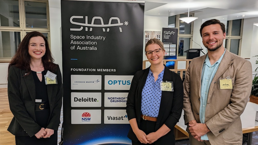 Two women and a man stand in front of a Space Industry Association of Australia sign.