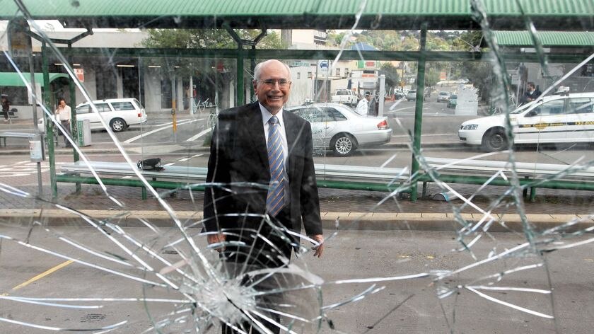 Prime Minister John Howard poses by a sheet of shattered glass