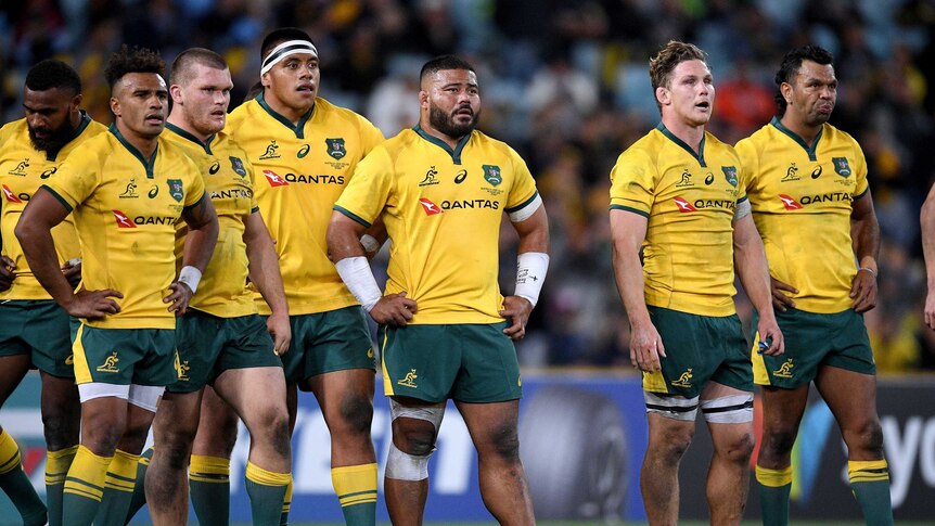 Rugby players in yellow shirts stand with their hands on their hips
