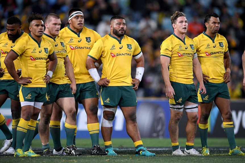 Rugby players in yellow shirts stand with their hands on their hips