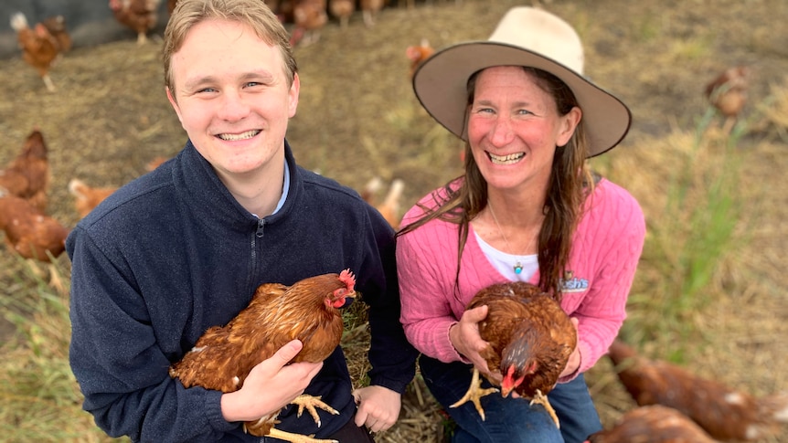 A son and his mum sitting in a field, holding hens.