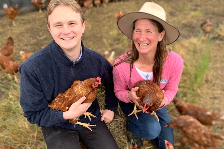 A son and his mum sitting in a field, holding hens.