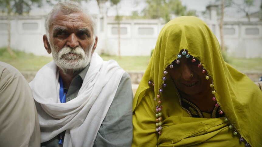 A Pakistani man and a woman in a yellow veil enter a court room.