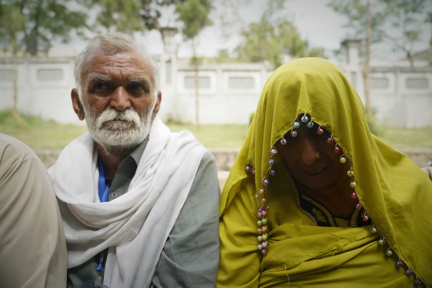 A Pakistani man and a woman in a yellow veil enter a court room.