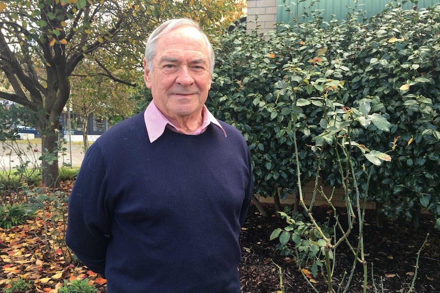 A man stands in front of rose bushes