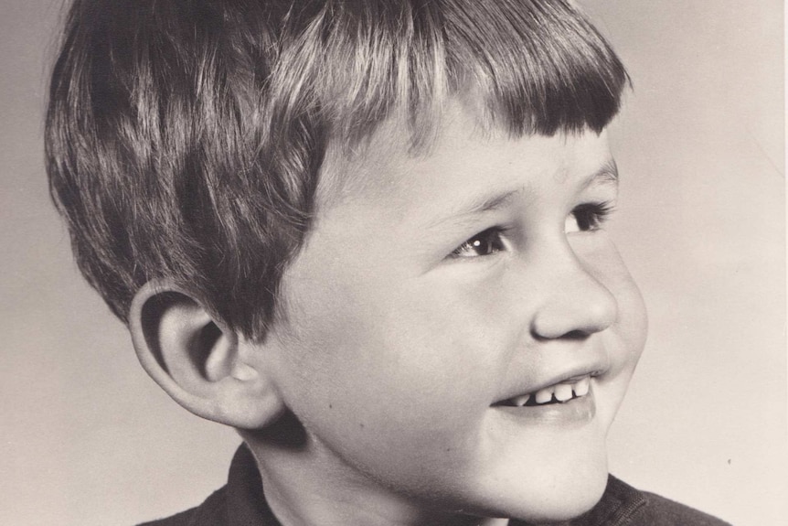 A young boy has his head turned slightly and smiles.
