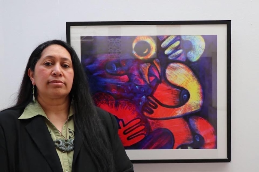 Maori woman stands next to an art work. 