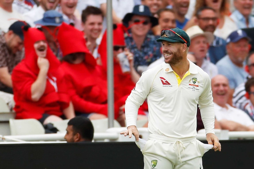 David Warner smiles while holding his empty pockets out for the crowd to see.