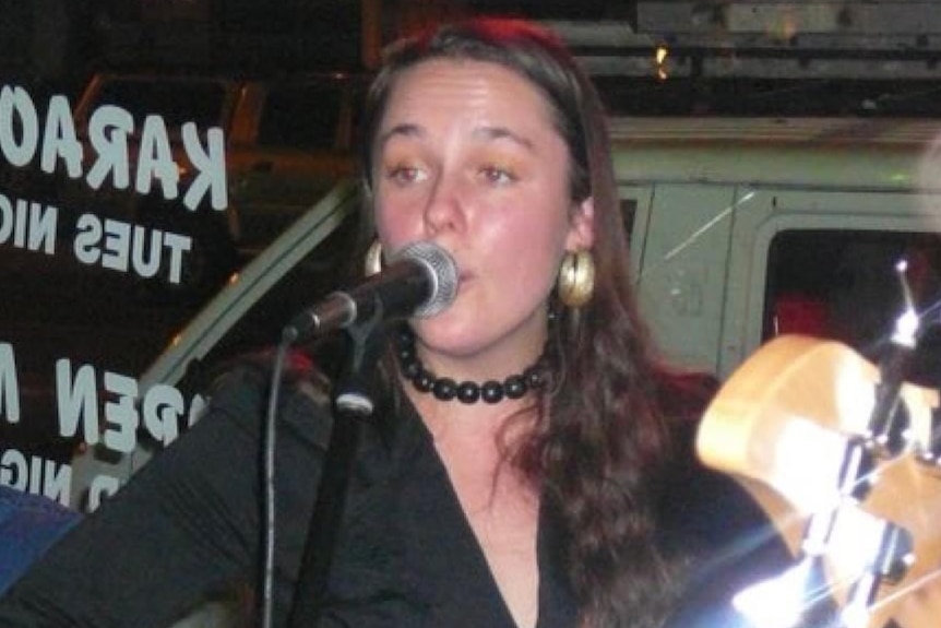 a woman singing into a microphone holding a guitar.