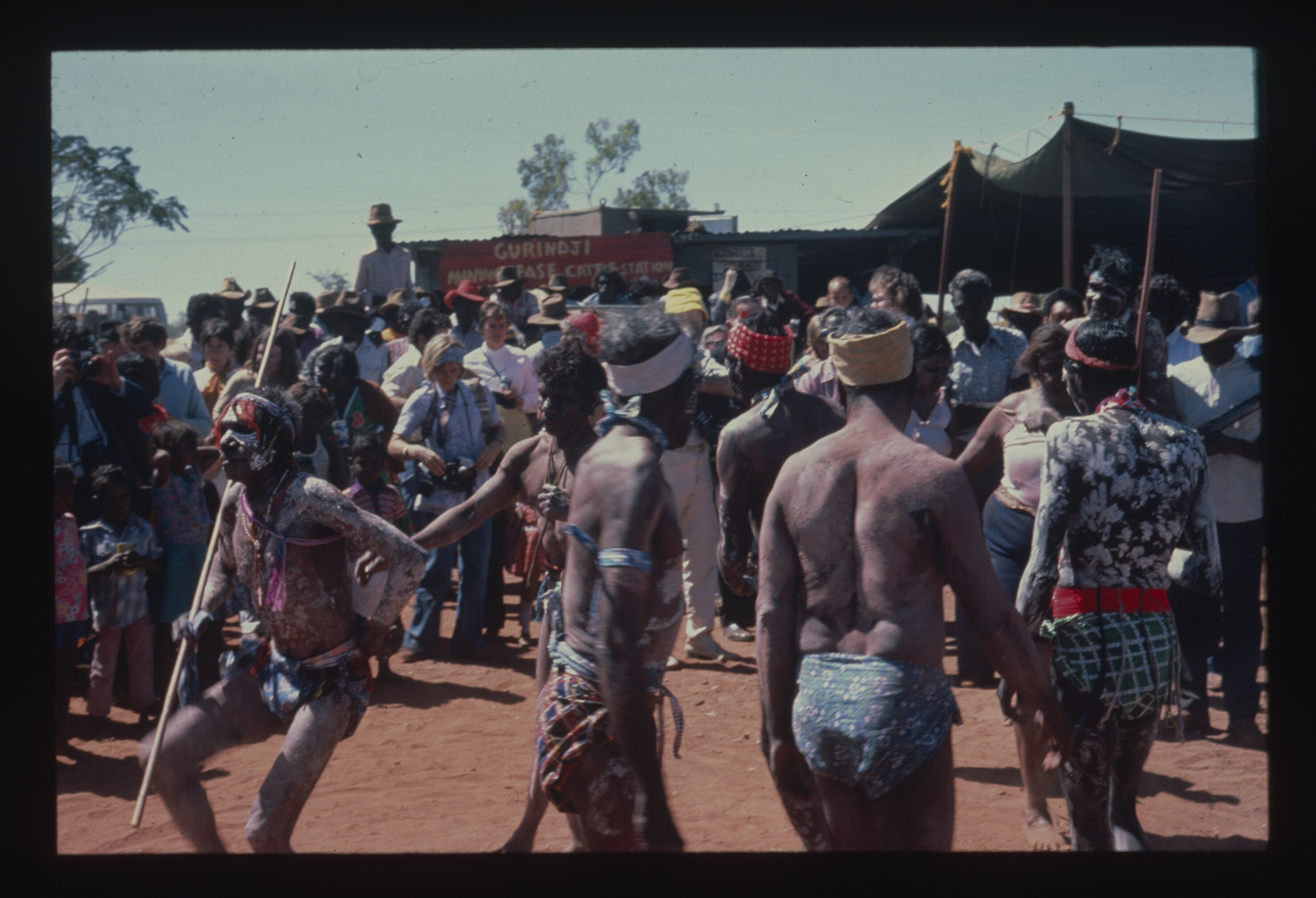 A group of Aboriginal people performing cultural dances, with crowd of photographers and journalists watching. 