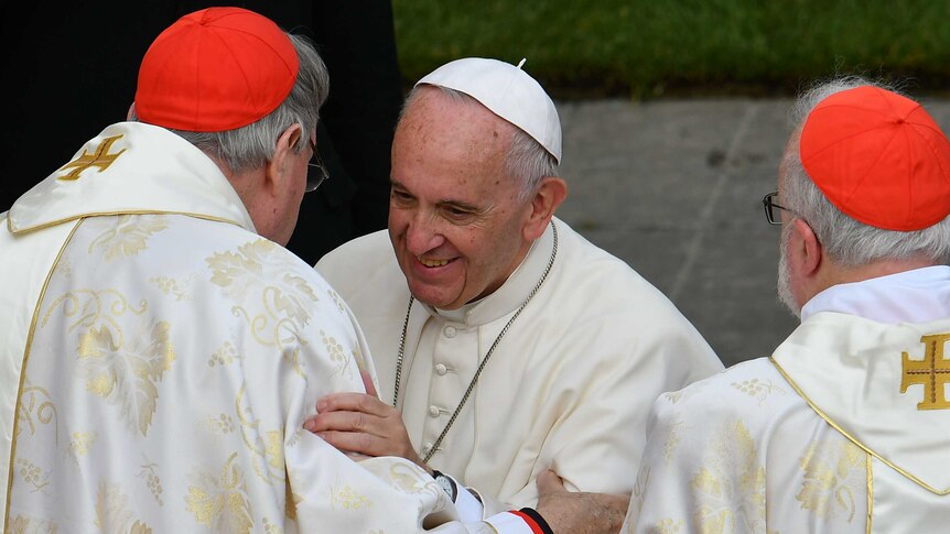 Cardinal George Pell and Pope Francis, who wear white religious robes, smile and embrace.