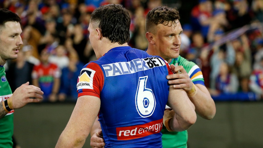 A young man in a green jersey pats another young man in a blue jersey on the back after a rugby league game.