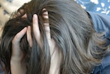 A young woman rests her head in her hands in a depressed pose