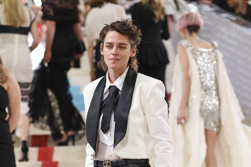 Kristen Stewart wears a white suit jacket with a black lapel and black suit pants.