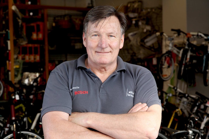 A man in a grey shirt surrounded by bicycles.