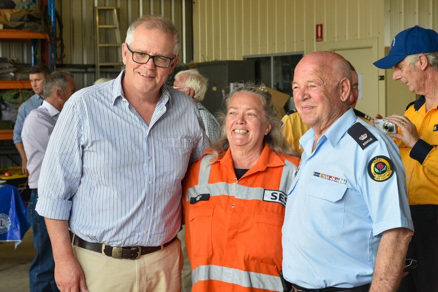 Scott Morrison stands with his arm around a woman in SES uniform next to a man in a blue uniform  