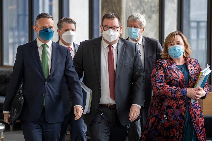 A group of middle aged men and a woman in professional business attire wearing COVID masks