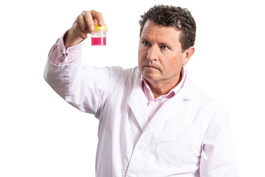 A man in a lab coat holds a beaker with red liquid
