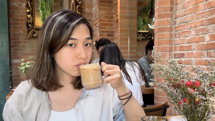 A woman with short black hair sips a coffee. 