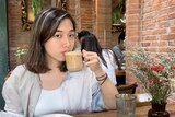 A woman with short black hair sips a coffee. 