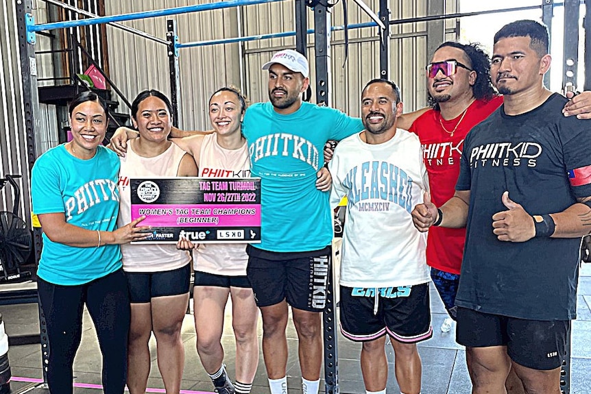 A group of Pacific Islanders stand together embracing each other in a gym setting