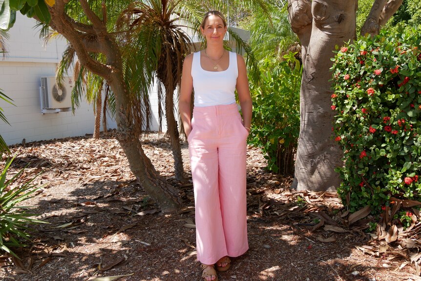 Exmouth chamber of commerce chief standing by some trees. She is wearing pink and a white tank top.