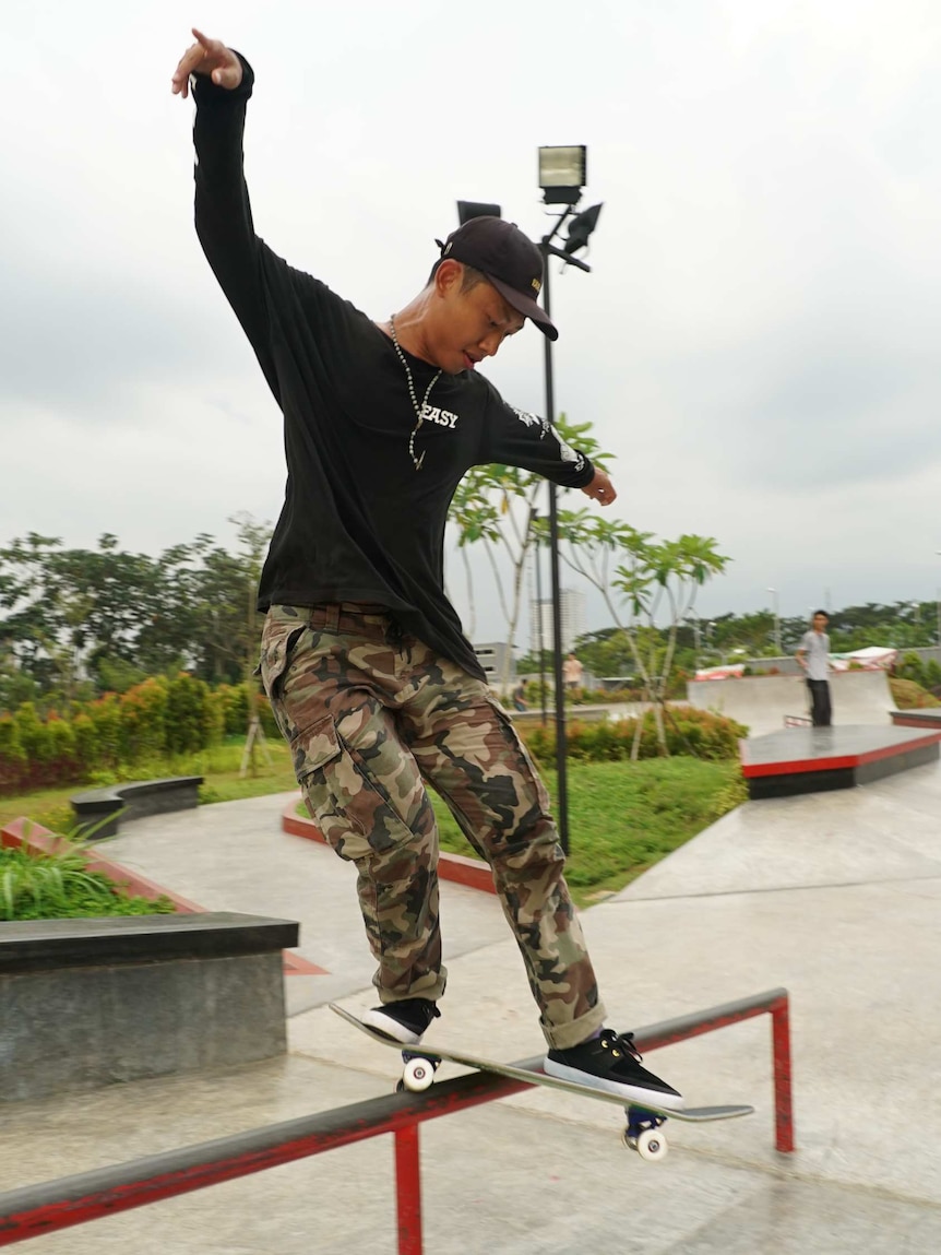 Indonesian skateboarder Gregorius Aldwin, he is balancing on his board as it slides down a rail.