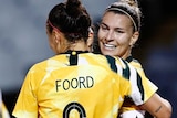 Steph Catley and Caitlin Foord hug in celebration. Hayley Raso jogs over to join them.