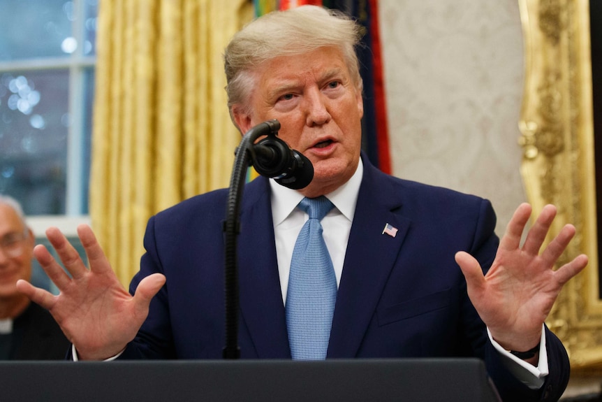 Donald Trump raises his hands as he speaks at a microphone