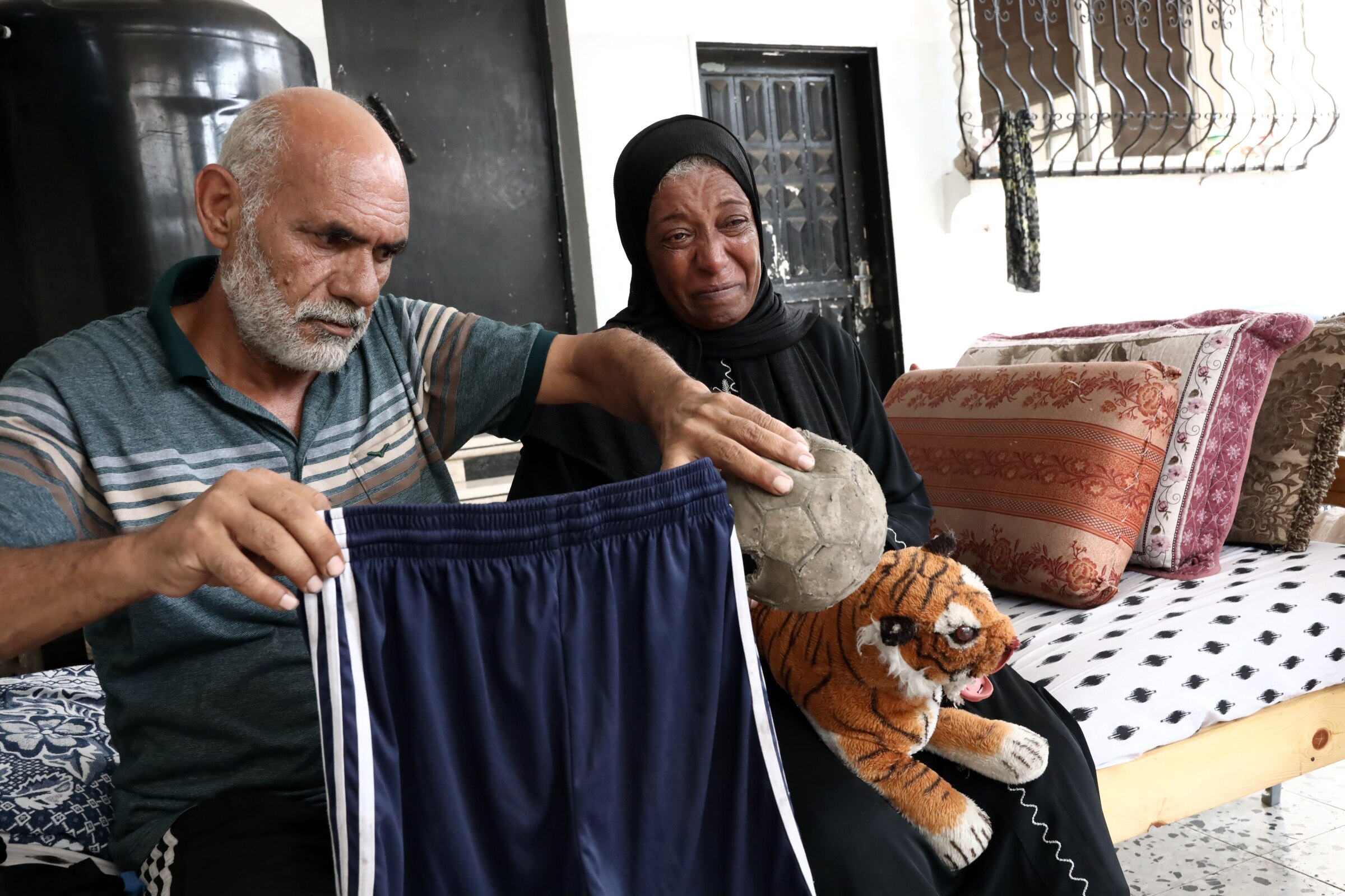 A father and mother sitting together, looking upset and holding various items of their son's.