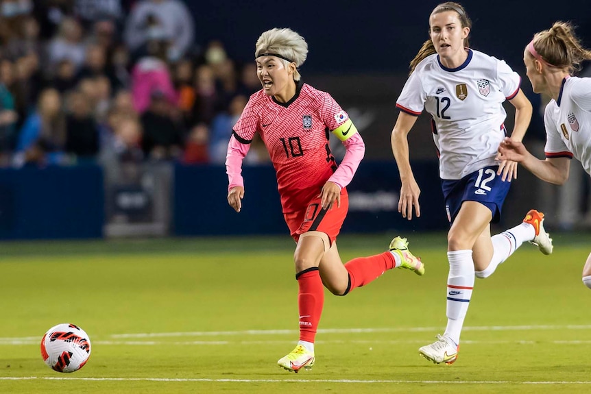 Ji So-yun carries the ball at her feet, pursued by two opposition players