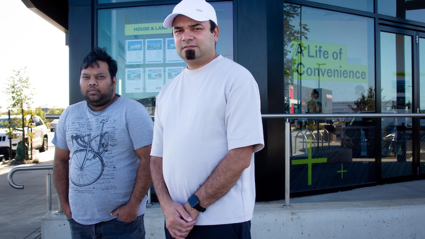 Two men stand in front of a building selling land with the sign 'a life of convenience'