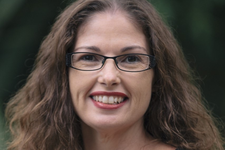 A Caucasian woman wearing thin rectangular glasses smiling in a professional photo 