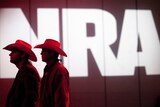 Two men with cowboy hats stand in front of a sign saying NRA.