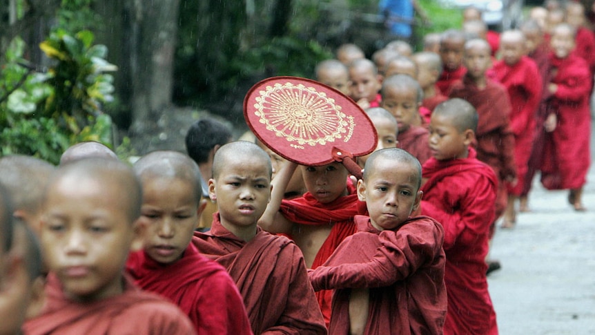 A group of young Buddhist monks walk in rain to collect offerings in the poor neighbourhood of Yangon.