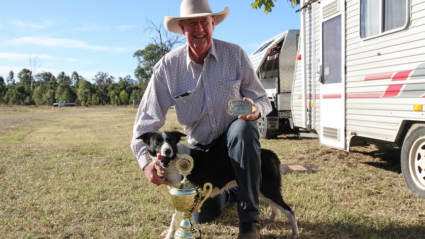 Dick Chapman kneels with his dog Panda while holding a belt buckle and trophy.