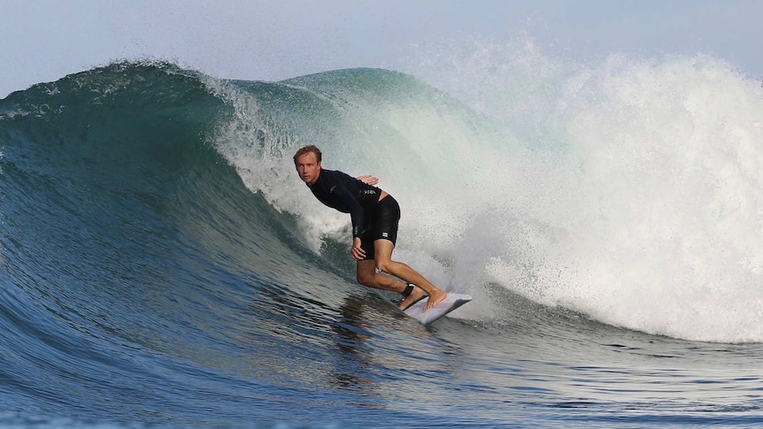 A young blonde surfer rides a wave with the water crashing behind him.