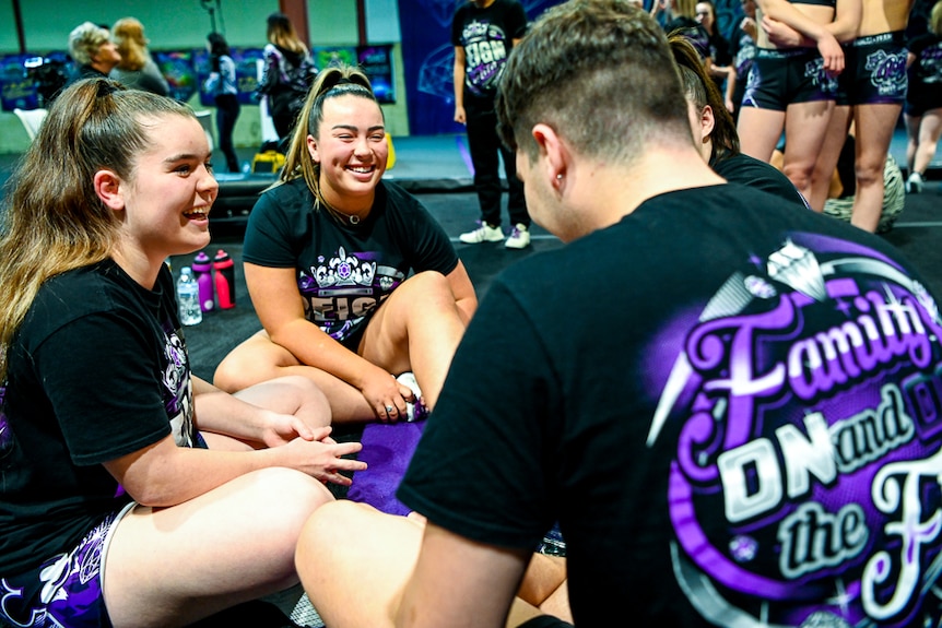 A group of athletes sit on the floor and laugh at the gym.