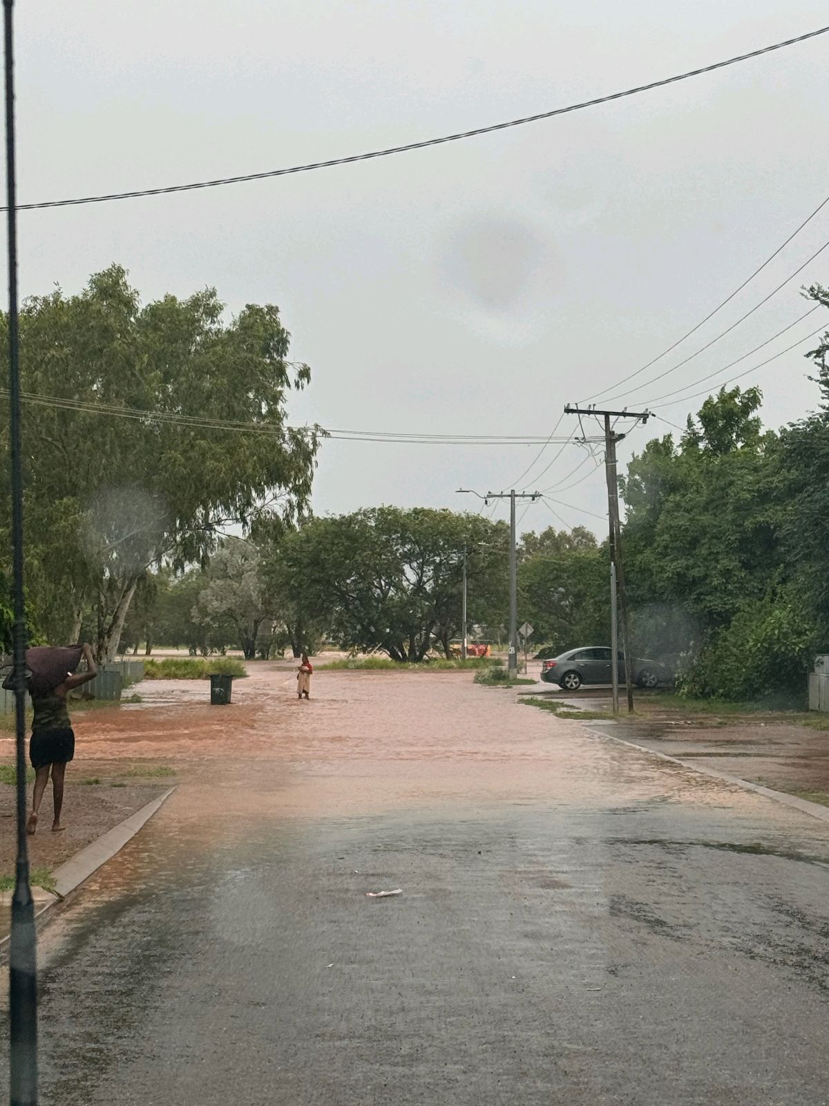 A person stands in brown flood waters on a road