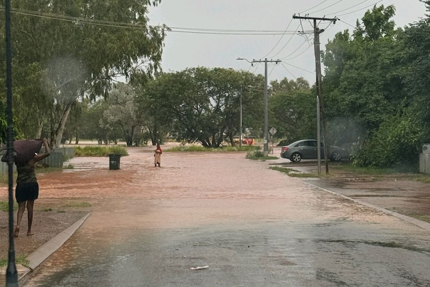 A person stands in brown flood waters on a road