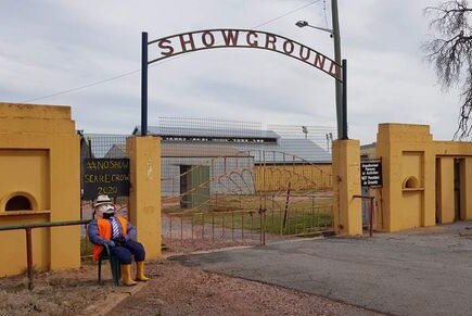 scarecrow in high vis, tie, hat and boots sits on chair out front showgrounds