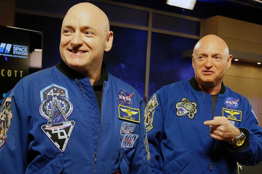 Scott and Mark Kelly sit next to each other, wearing matching dark blue NASA jackets